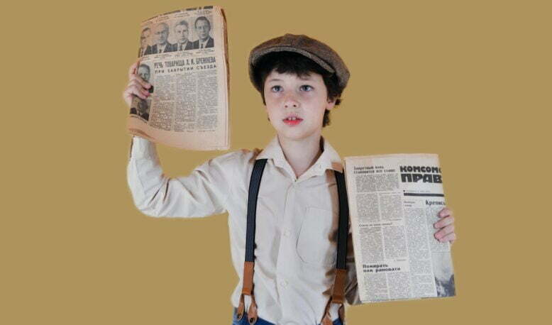 stylish boy showing aged newspapers against yellow background